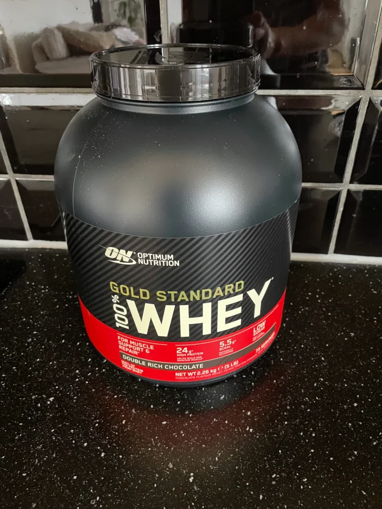 Burk med Gold Standard Whey proteinpulver i vit och röd design på svart bakgrund. Min egen åsikt, så är det bästa proteinpulvret 2025